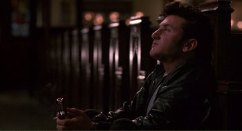 Movie still from “State of Grace” (1990), directed by Phil Joanou – A young man holding a bottle of beer in his hands; Medium shot, Low angle