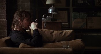 Movie still from “State of Grace” (1990), directed by Phil Joanou – A person sitting on a couch with a glass of water; Medium shot, Over the shoulder angle