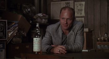 Movie still from “State of Grace” (1990), directed by Phil Joanou – A man sitting at a table next to a bottle of whiskey; Medium shot, Low angle
