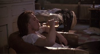 Movie still from “State of Grace” (1990), directed by Phil Joanou – A man sitting on top of a brown couch drinking a beer; Medium shot, High angle