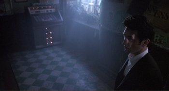 Movie still from “State of Grace” (1990), directed by Phil Joanou – A man in a suit and tie standing in a dark room; Medium shot, Low angle