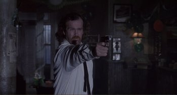 Movie still from “State of Grace” (1990), directed by Phil Joanou – A man holding a gun in a room; Medium shot, Over the shoulder angle