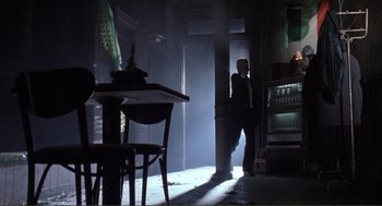 Movie still from “State of Grace” (1990), directed by Phil Joanou – A man standing in a dimly - lit room talking on a phone; Wide shot, Low angle