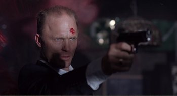 Movie still from “State of Grace” (1990), directed by Phil Joanou – A man holding a gun in a dark room; Close Up shot, Low angle