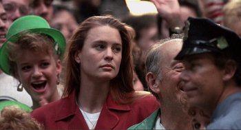 Movie still from “State of Grace” (1990), directed by Phil Joanou – A woman in a red jacket is standing in front of a crowd; Close Up shot, Over the shoulder angle