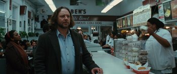 Movie still from “State of Play” (2009), directed by Kevin Macdonald – A man standing at a counter in front of a crowd; Medium shot, Over the shoulder angle