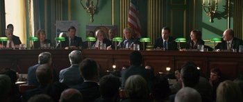 Movie still from “State of Play” (2009), directed by Kevin Macdonald – A group of men sitting at a table in front of an american flag; Wide shot, Over the shoulder angle