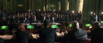 Movie still from “State of Play” (2009), directed by Kevin Macdonald – A group of people sitting in a room with green lamps; Extreme Wide shot, High angle