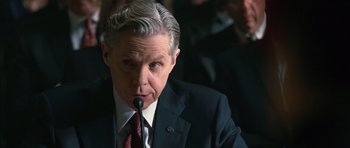 Movie still from “State of Play” (2009), directed by Kevin Macdonald – An older man wearing a suit and tie while speaking into a microphone; Close Up shot, Over the shoulder angle