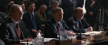 Movie still from “State of Play” (2009), directed by Kevin Macdonald – A man sitting at a conference table with a group of people behind him; Medium shot, Over the shoulder angle