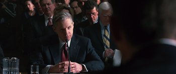 Movie still from “State of Play” (2009), directed by Kevin Macdonald – A man in a suit and tie sitting at a table with other people; Close Up shot, Over the shoulder angle