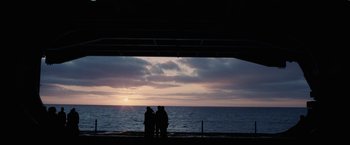 Movie still from “Stealth” (2005), directed by Rob Cohen – Three people standing on a pier watching the sun go down over the ocean; Extreme Wide shot, Over the shoulder angle