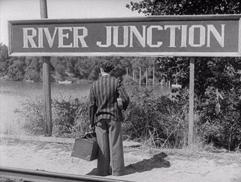 Movie still from “Steamboat Bill, Jr.” (1928), directed by Buster Keaton – An old photo of a man standing under a river junction sign; Wide shot, High angle