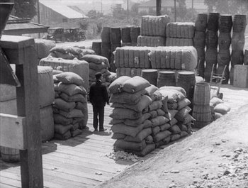 Movie still from “Steamboat Bill, Jr.” (1928), directed by Buster Keaton – A man standing in front of a pile of bags; Extreme Wide shot, High angle