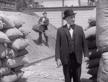 Movie still from “Steamboat Bill, Jr.” (1928), directed by Buster Keaton – An old photo of a man in a suit and a hat; Medium shot, Over the shoulder angle