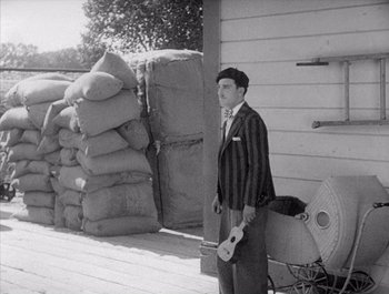 Movie still from “Steamboat Bill, Jr.” (1928), directed by Buster Keaton – A man standing in front of a pile of bags; Wide shot, Over the shoulder angle