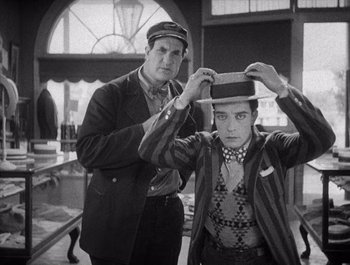 Movie still from “Steamboat Bill, Jr.” (1928), directed by Buster Keaton – A man and a boy are putting on a hat; Medium shot, Over the shoulder angle