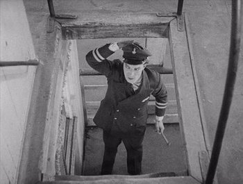 Movie still from “Steamboat Bill, Jr.” (1928), directed by Buster Keaton – An old photo of a man in a uniform standing on stairs; Medium shot, High angle