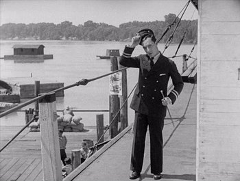 Movie still from “Steamboat Bill, Jr.” (1928), directed by Buster Keaton – An old photo of a man in a uniform standing on a pier; Medium shot, Low angle