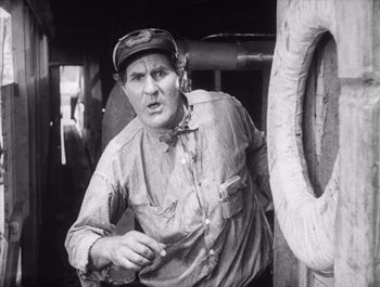 Movie still from “Steamboat Bill, Jr.” (1928), directed by Buster Keaton – An older man wearing a hat standing next to a boat; Medium shot, Low angle