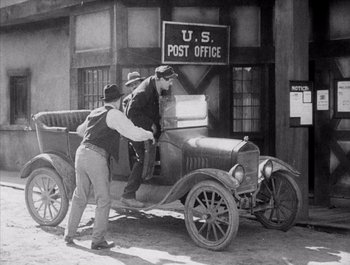 Movie still from “Steamboat Bill, Jr.” (1928), directed by Buster Keaton – Two men standing next to an old car; Wide shot, Low angle