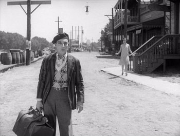 Movie still from “Steamboat Bill, Jr.” (1928), directed by Buster Keaton – An old black and white photo of a man and woman walking down a street; Medium shot, Over the shoulder angle