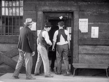 Movie still from “Steamboat Bill, Jr.” (1928), directed by Buster Keaton – A group of men standing in front of a building; Wide shot, Over the shoulder angle