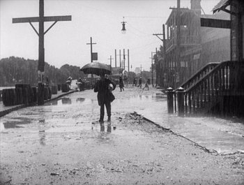 Movie still from “Steamboat Bill, Jr.” (1928), directed by Buster Keaton – A person with an umbrella walking down a street; Wide shot, Low angle