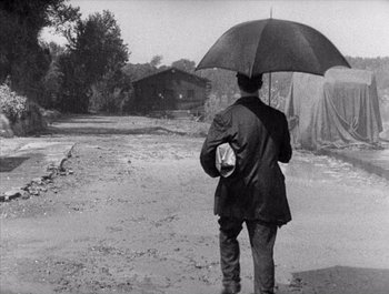 Movie still from “Steamboat Bill, Jr.” (1928), directed by Buster Keaton – A man holding an umbrella while standing in the rain; Wide shot, High angle