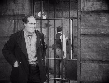 Movie still from “Steamboat Bill, Jr.” (1928), directed by Buster Keaton – A black and white photo of a man standing in front of a jail cell; Medium shot, Over the shoulder angle
