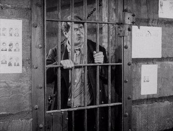 Movie still from “Steamboat Bill, Jr.” (1928), directed by Buster Keaton – A black and white photo of a man behind bars; Medium shot, High angle