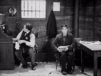 Movie still from “Steamboat Bill, Jr.” (1928), directed by Buster Keaton – A man sitting on a chair next to another man; Medium shot, High angle