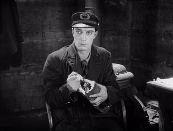 Movie still from “Steamboat Bill, Jr.” (1928), directed by Buster Keaton – A black and white photo of a man eating a sandwich; Medium shot, High angle