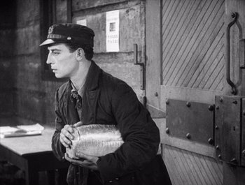 Movie still from “Steamboat Bill, Jr.” (1928), directed by Buster Keaton – A man holding a metal container in his hands; Medium shot, High angle