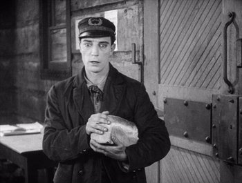 Movie still from “Steamboat Bill, Jr.” (1928), directed by Buster Keaton – A man holding a loaf of bread in his hands; Medium shot, High angle