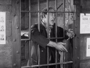 Movie still from “Steamboat Bill, Jr.” (1928), directed by Buster Keaton – A black and white photo of a man behind bars; Medium shot, High angle
