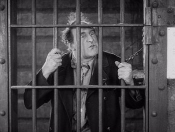 Movie still from “Steamboat Bill, Jr.” (1928), directed by Buster Keaton – An old man is standing behind bars in a jail cell; Medium shot, High angle
