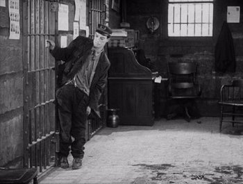 Movie still from “Steamboat Bill, Jr.” (1928), directed by Buster Keaton – A man leaning against a wall in an old jail cell; Wide shot, High angle