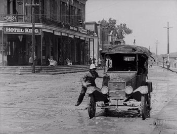 Movie still from “Steamboat Bill, Jr.” (1928), directed by Buster Keaton – An old photo of an old car in the middle of the street; Wide shot, High angle