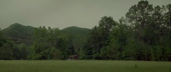 Movie still from “Still” (2018), directed by Takashi Doscher – A field with trees and a house in the background; Extreme Wide shot, Low angle