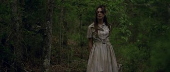 Movie still from “Still” (2018), directed by Takashi Doscher – A woman standing in the woods wearing a striped dress; Medium shot, Over the shoulder angle