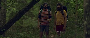 Movie still from “Still” (2018), directed by Takashi Doscher – Two bearded men with backpacks in the woods; Medium shot, Low angle