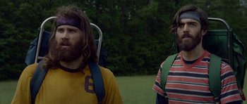 Movie still from “Still” (2018), directed by Takashi Doscher – A man with long hair is standing next to another man with long hair; Medium shot, Low angle