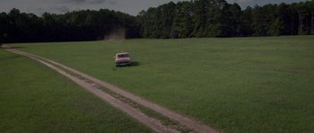Movie still from “Still” (2018), directed by Takashi Doscher – An old car is driving through a grassy field; Extreme Wide shot, High angle