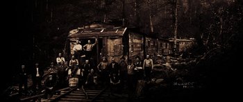 Movie still from “Still” (2018), directed by Takashi Doscher – A group of men standing in front of an old train car; Extreme Wide shot, High angle