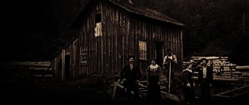 Movie still from “Still” (2018), directed by Takashi Doscher – A man and a woman standing in front of a wooden house; Extreme Wide shot, Low angle