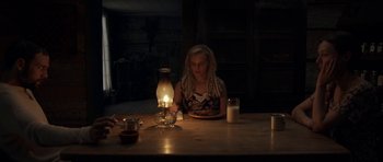Movie still from “Still” (2018), directed by Takashi Doscher – A woman sitting at a table in front of an oil lamp; Medium shot, High angle
