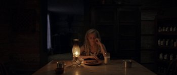 Movie still from “Still” (2018), directed by Takashi Doscher – A woman sitting at a table in a dimly - lit room; Medium shot, High angle