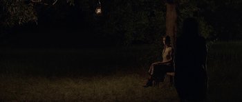 Movie still from “Still” (2018), directed by Takashi Doscher – A woman sitting on a bench in the dark; Wide shot, High angle
