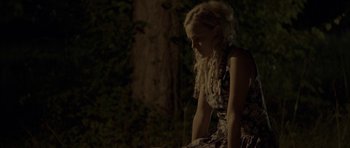Movie still from “Still” (2018), directed by Takashi Doscher – A girl sitting in the dark in front of a tree; Medium shot, High angle